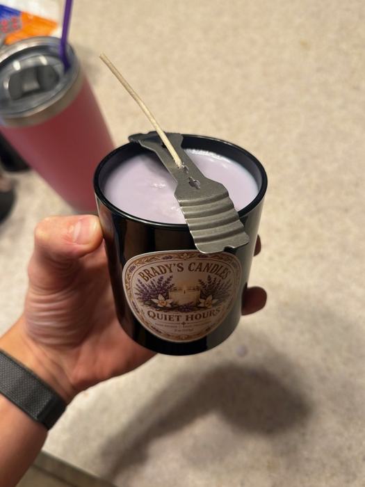 Wax being poured into a black glass jar with the wick held centered
